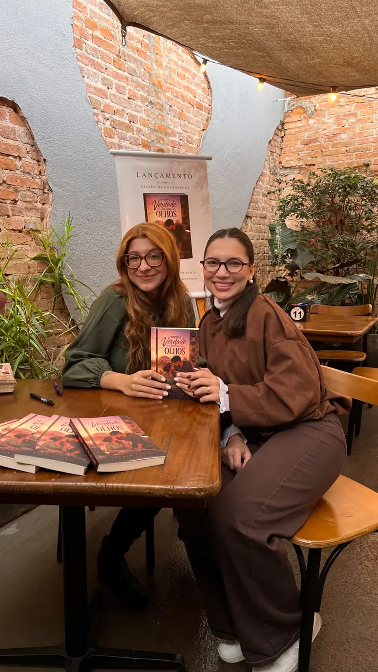 Esther Faria com uma leitora segurando o livro na mesa de autógrafos