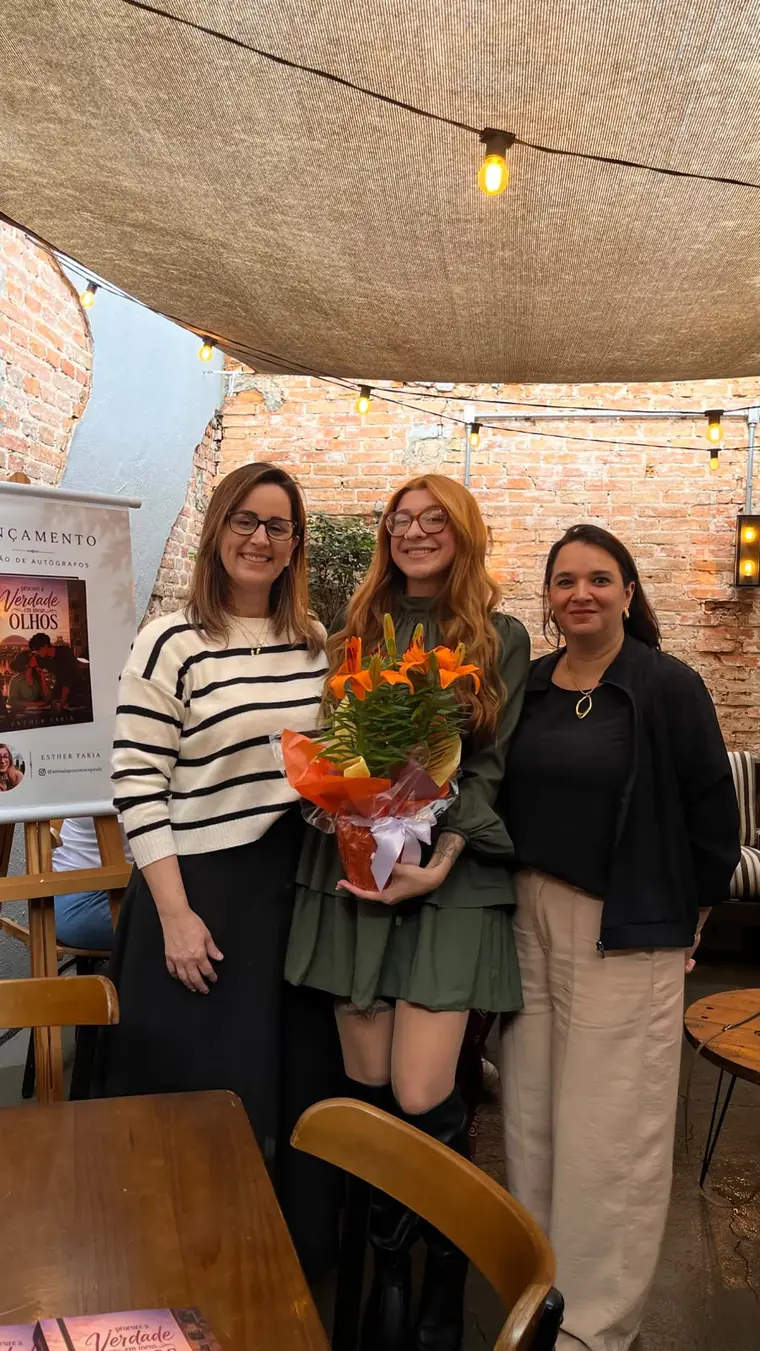 Esther Faria entre duas convidadas com um buquê de flores no lançamento