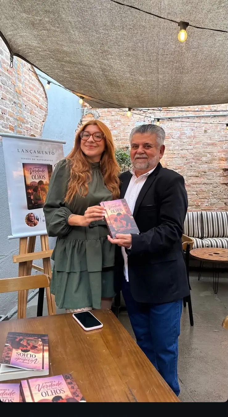 Esther Faria com um convidado segurando o livro no lançamento